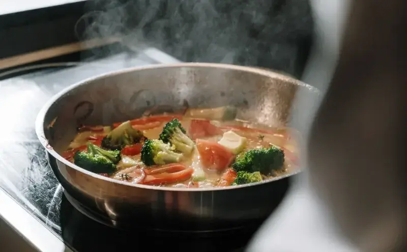Verduras y hierbas cocinándose en una sartén, con vapor.