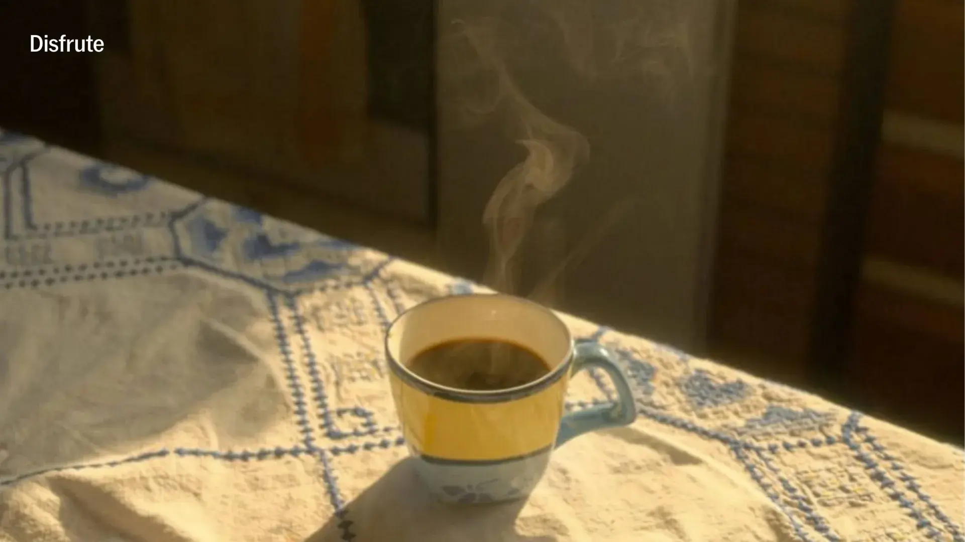 Una taza de café sobre un mantel bordado, junto a una ventana con luz de mañana.
