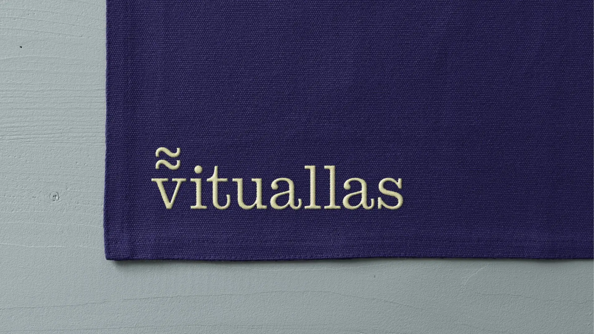 Logotipo de Vituallas bordado en crema sobre una tela índigo.